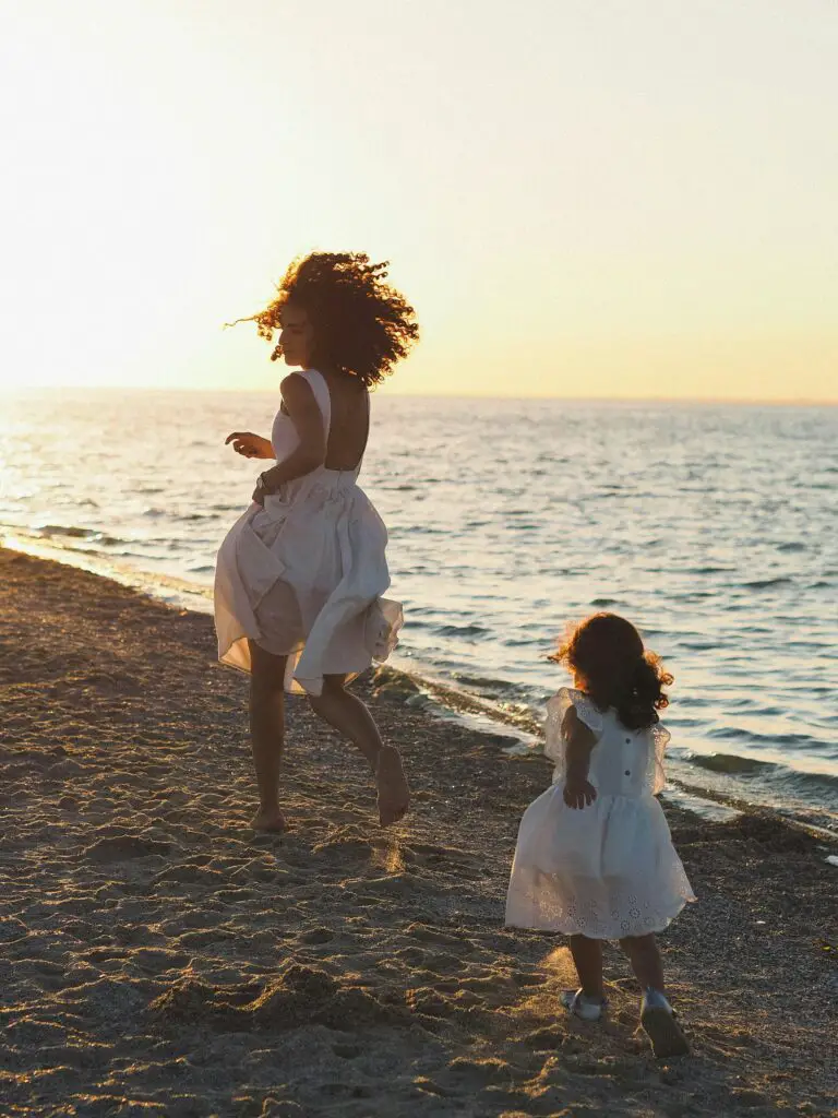 Heartwarming scene of a mother and daughter running along the beach at sunset in white dresses.