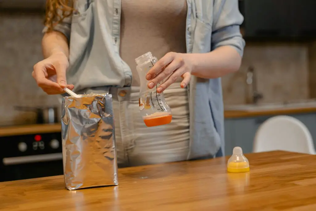 A parent prepares a baby bottle with formula on a wooden table in a cozy kitchen setting.