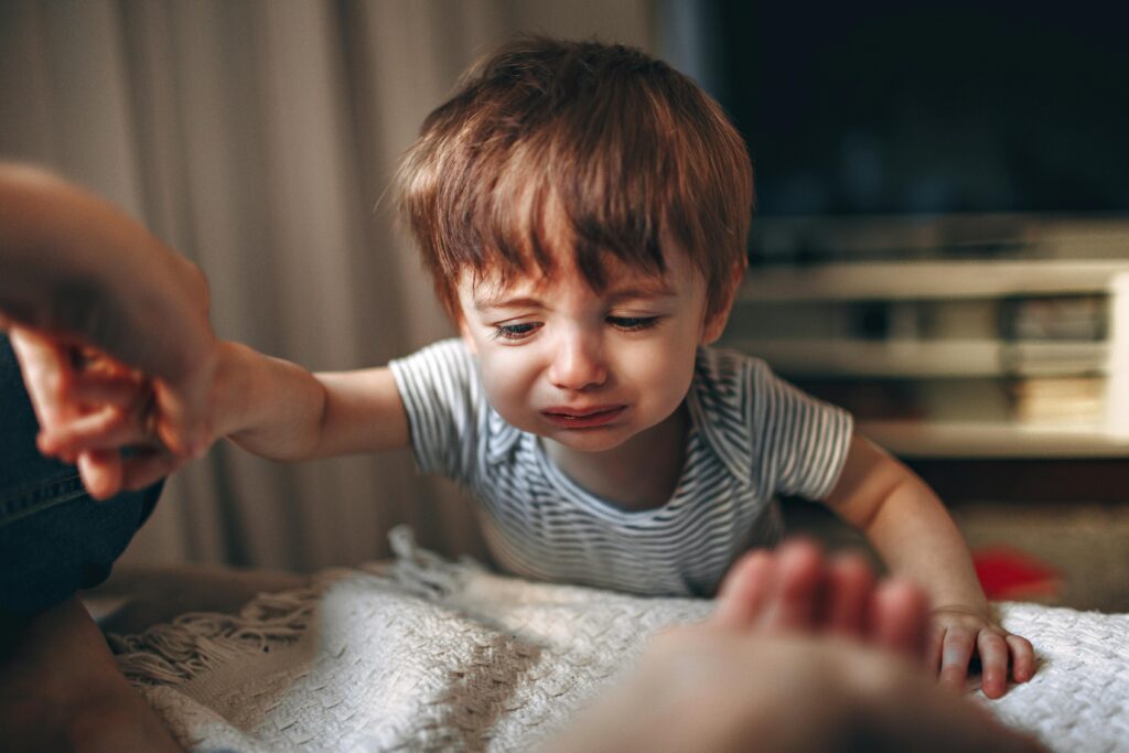 A close-up of an upset Caucasian toddler reaching out while crying indoors, capturing raw emotion.