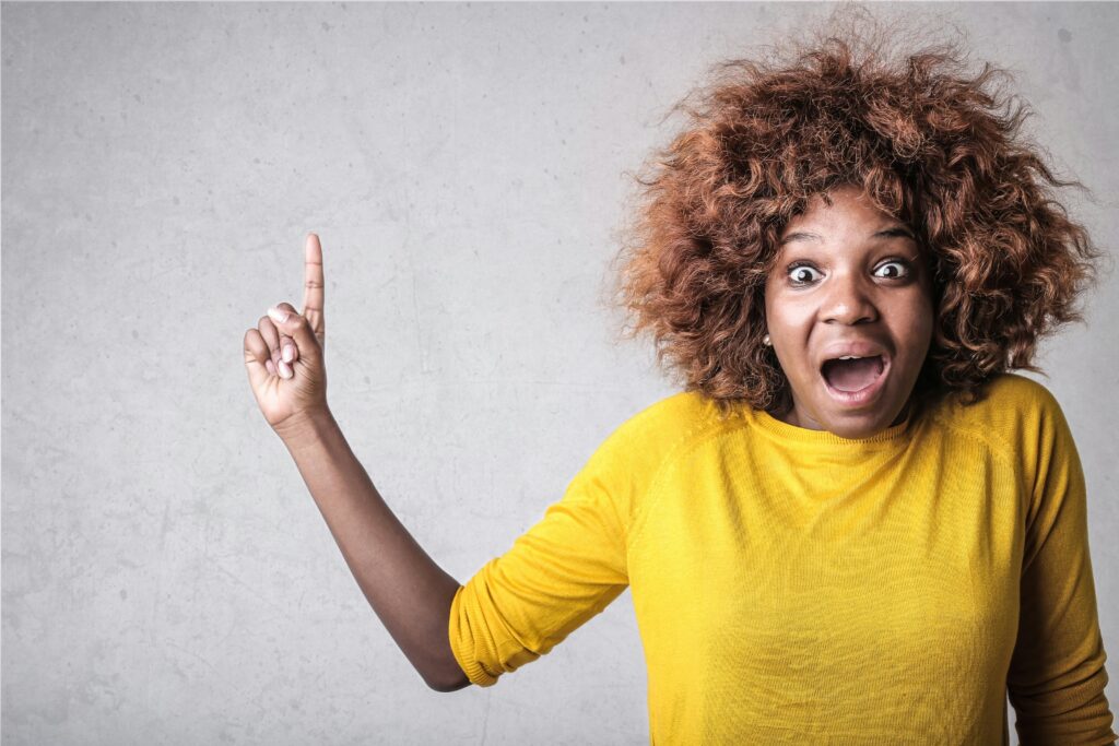 Portrait of a joyful woman pointing upwards, expressing excitement in a studio setting.