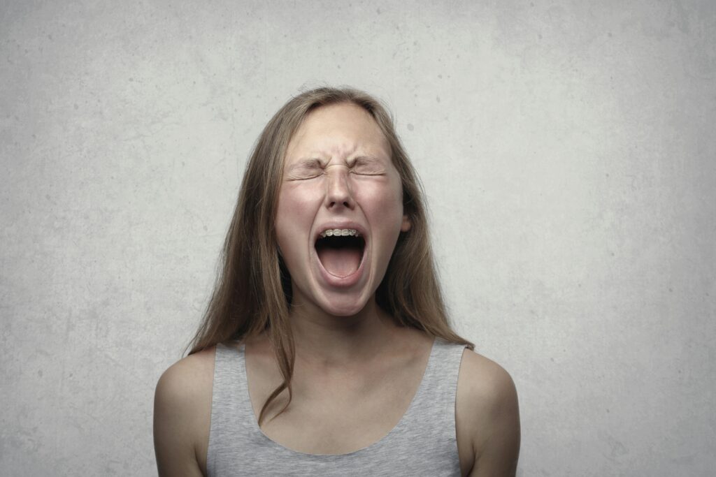 Young woman screaming with emotion, showing braces, against a gray backdrop.